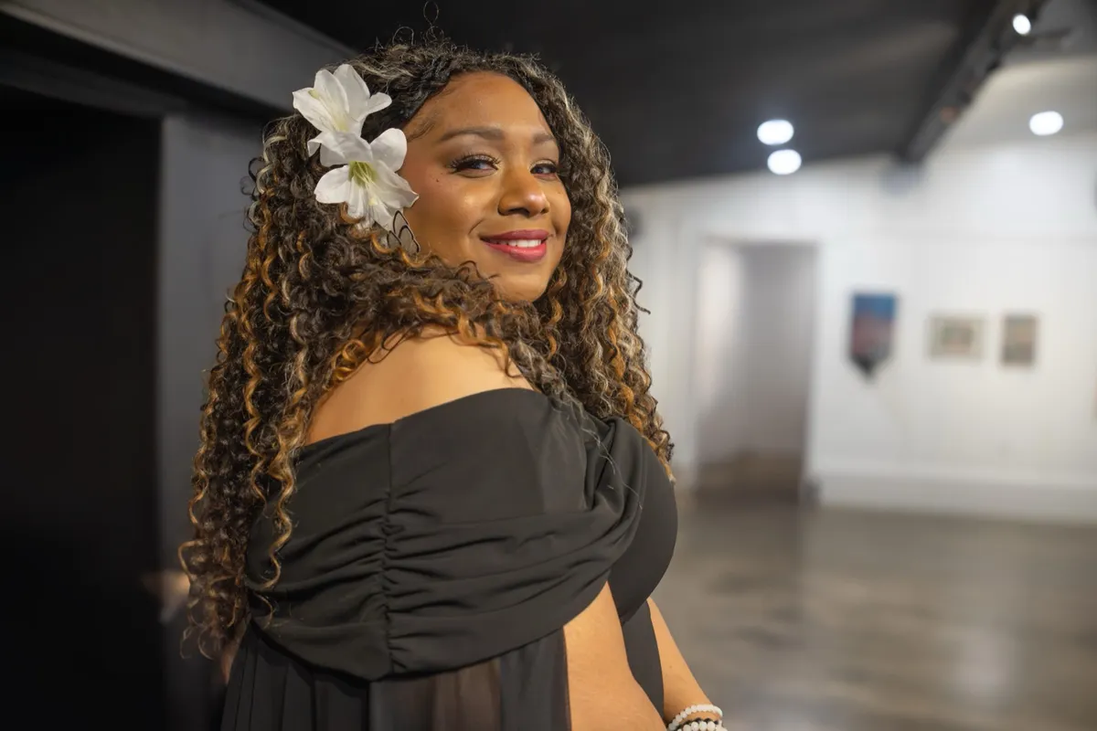 Andrea “Vocab” Sanderson smiling in a gallery, wearing a white flower in her hair