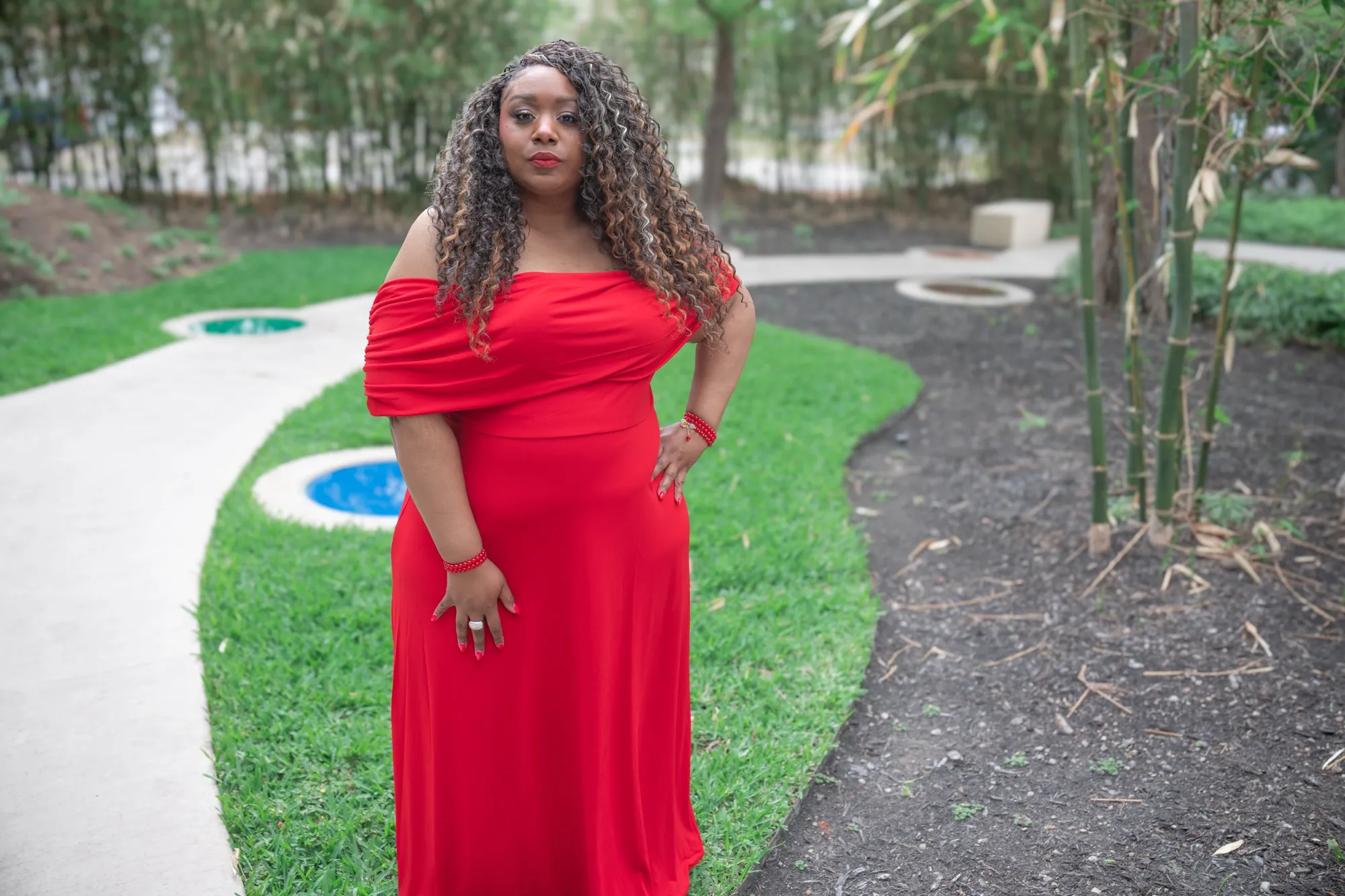 Andrea “Vocab” Sanderson standing on a garden path in a red gown, hand on hip