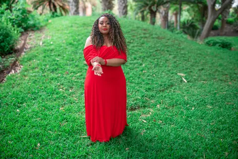 Andrea “Vocab” Sanderson on a grassy hill among palm trees, wearing a red gown