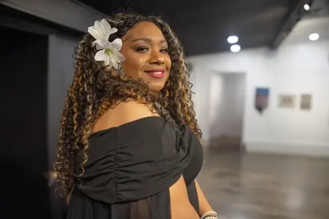 Andrea “Vocab” Sanderson smiling in a gallery, wearing a white flower in her hair