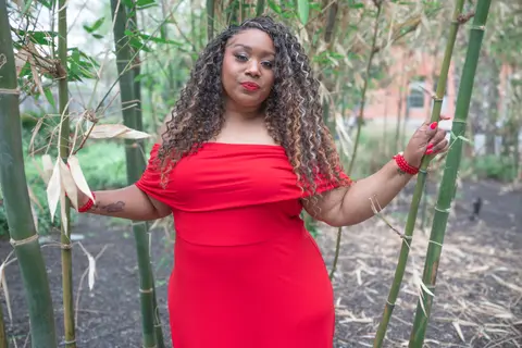 Andrea “Vocab” Sanderson in a red dress standing among bamboo